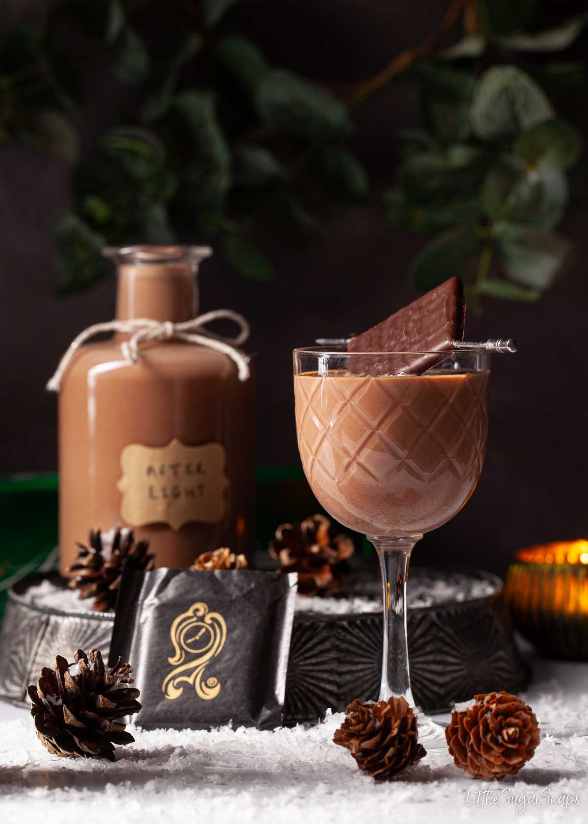 A glass of chocolate mint liqueur with an After Eight garnish. In a festive setting.