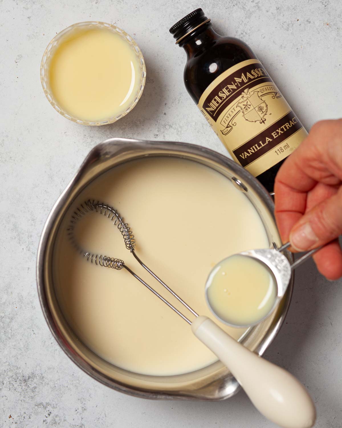 A person adding condensed milk to a pan of cream.