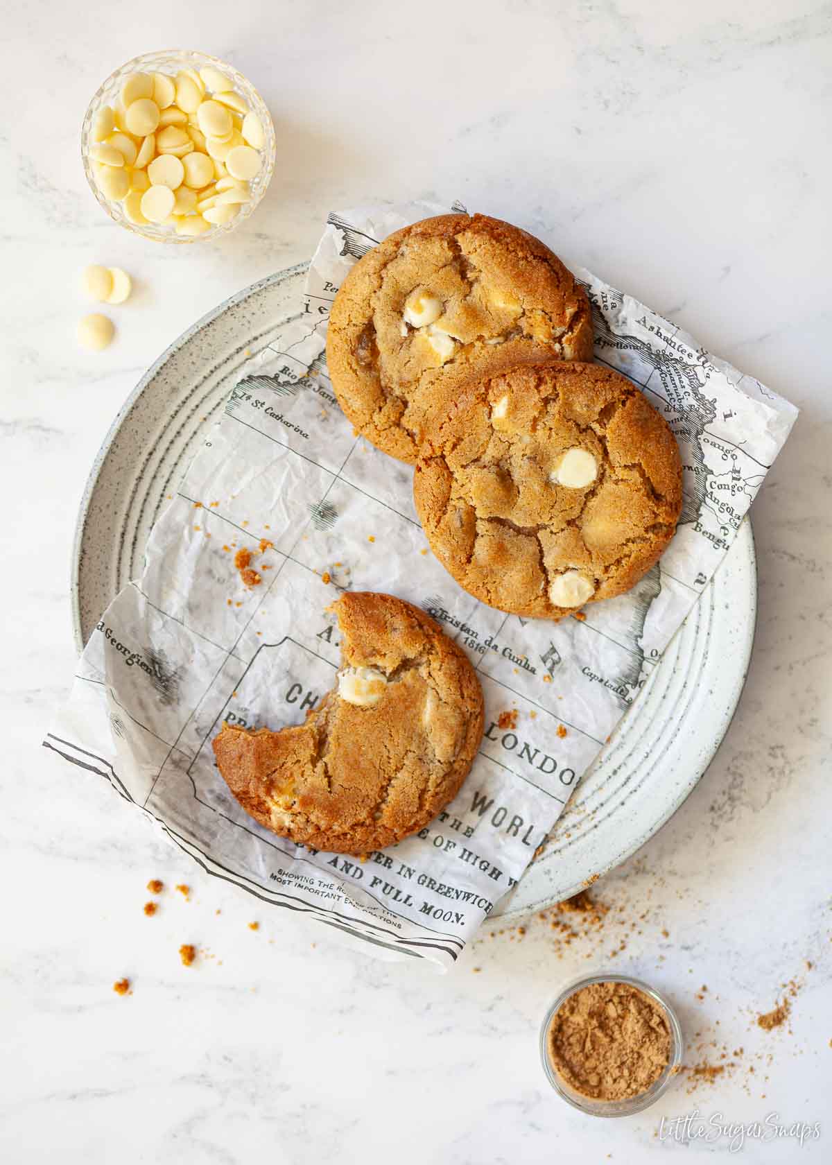 Three white chocolate stem ginger cookies on a plate with a bite taken out of one.