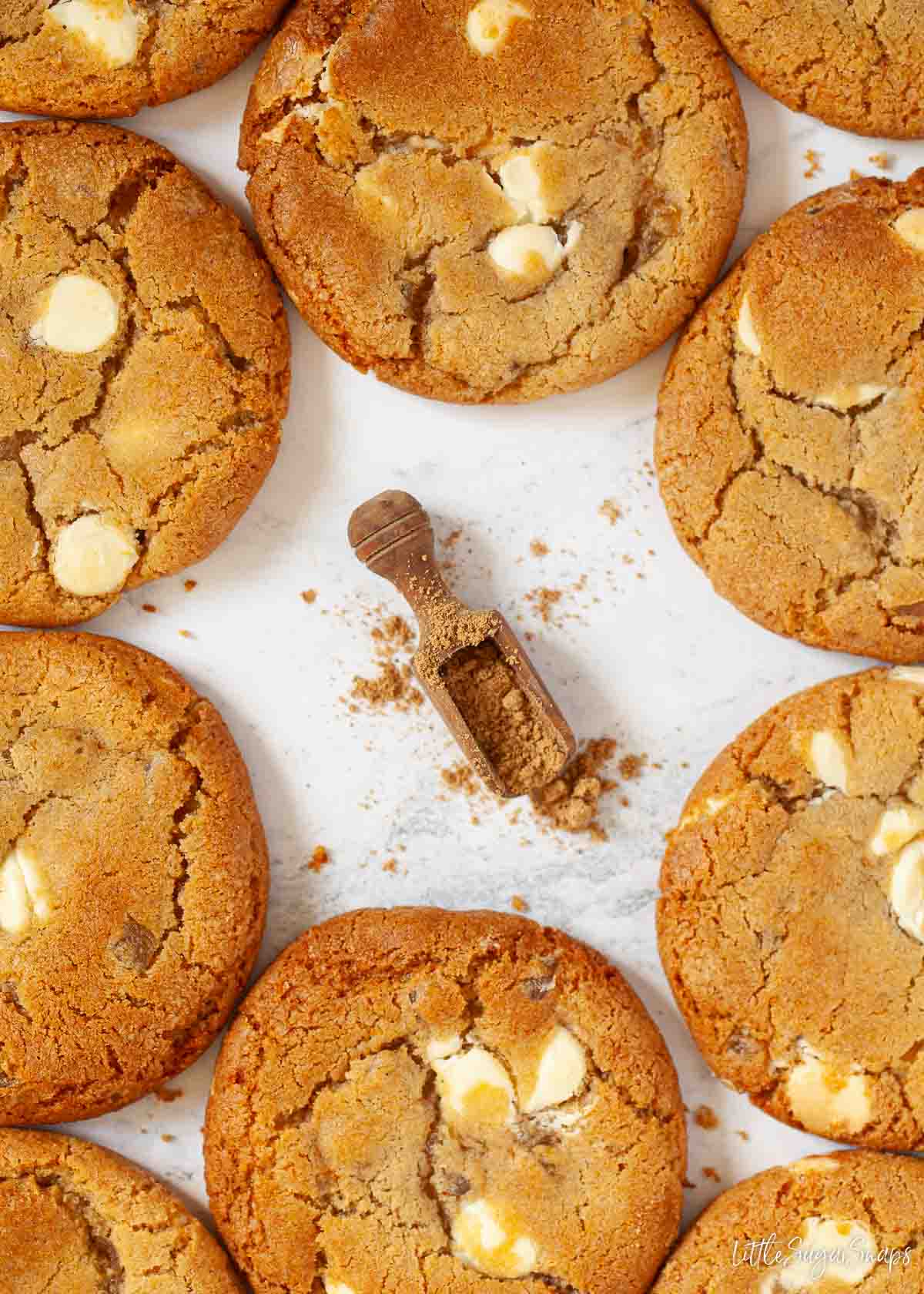 Ground ginger on a wooden scoop surrounded by white chocolate ginger cookies.
