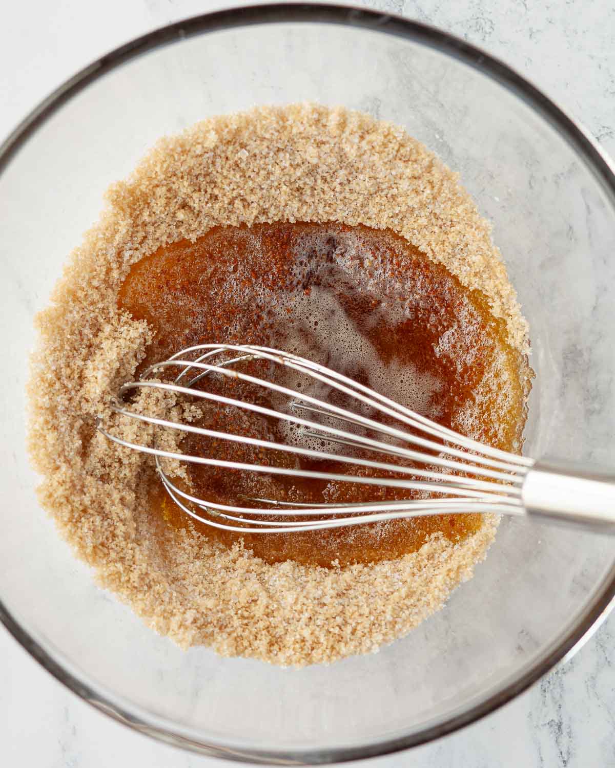 Browned butter poured over sugar in a mixing bowl with a balloon whisk resting in it.