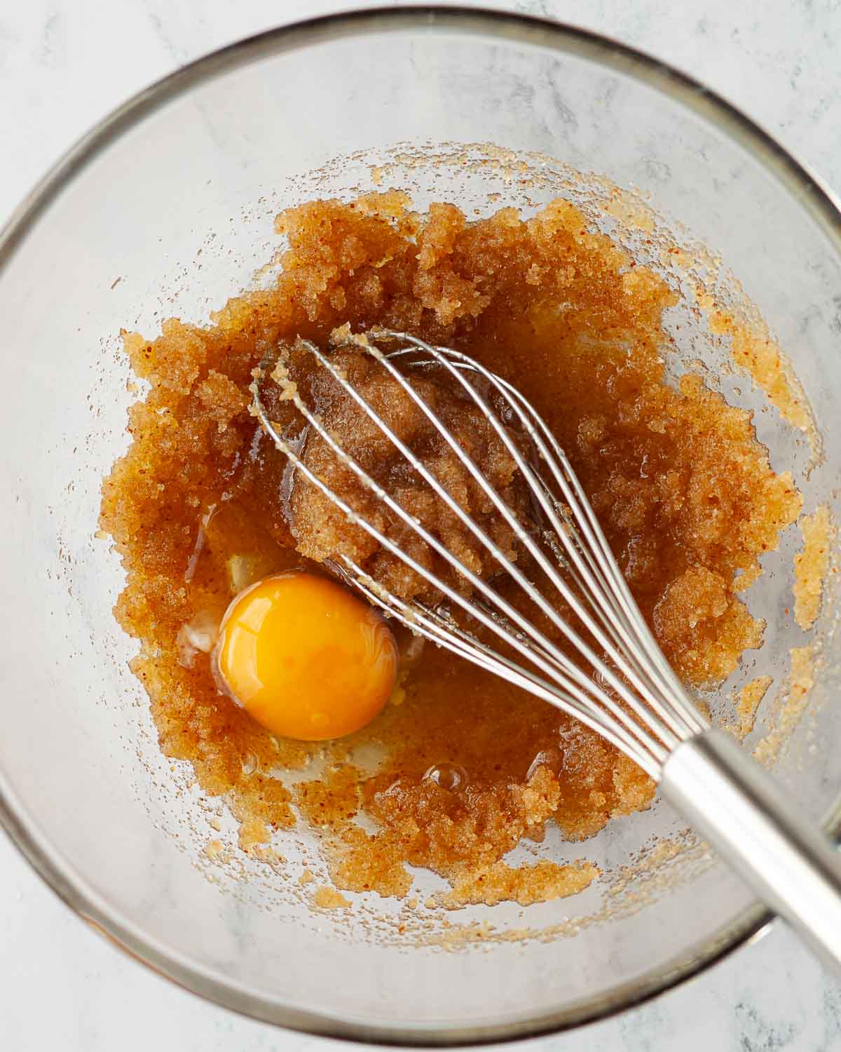Browned sugar whisked into sugar with an egg about to be mixed in.