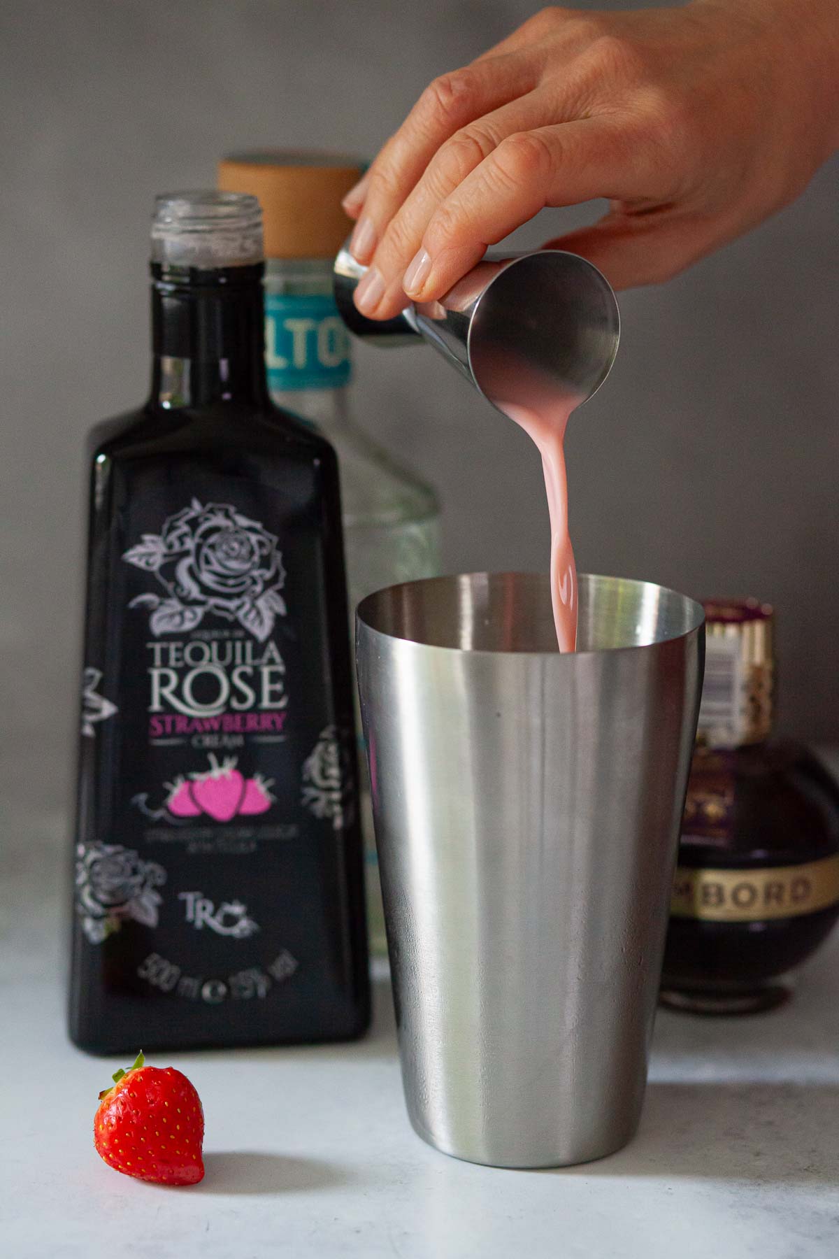Person pouring strawberry cream liqueur into a cocktail shaker