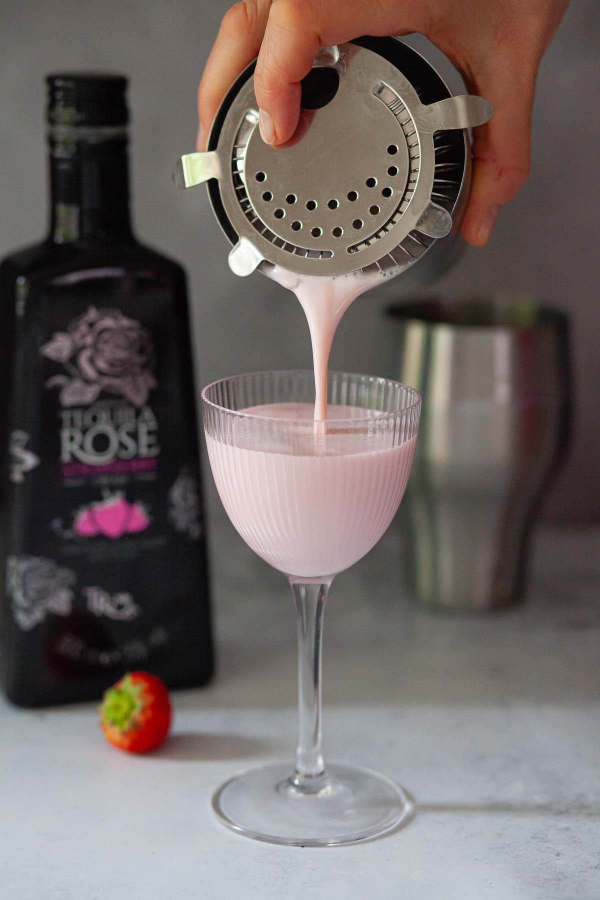 Person pouring a creamy strawberry liqueur cocktail into a ribbed glass.