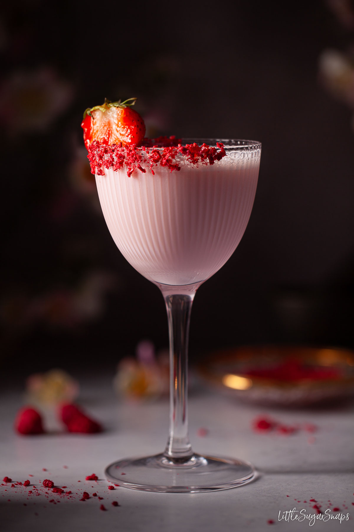 A Tequila Rose cocktail with strawberry garnish and freeze-dried raspberry glass rim.