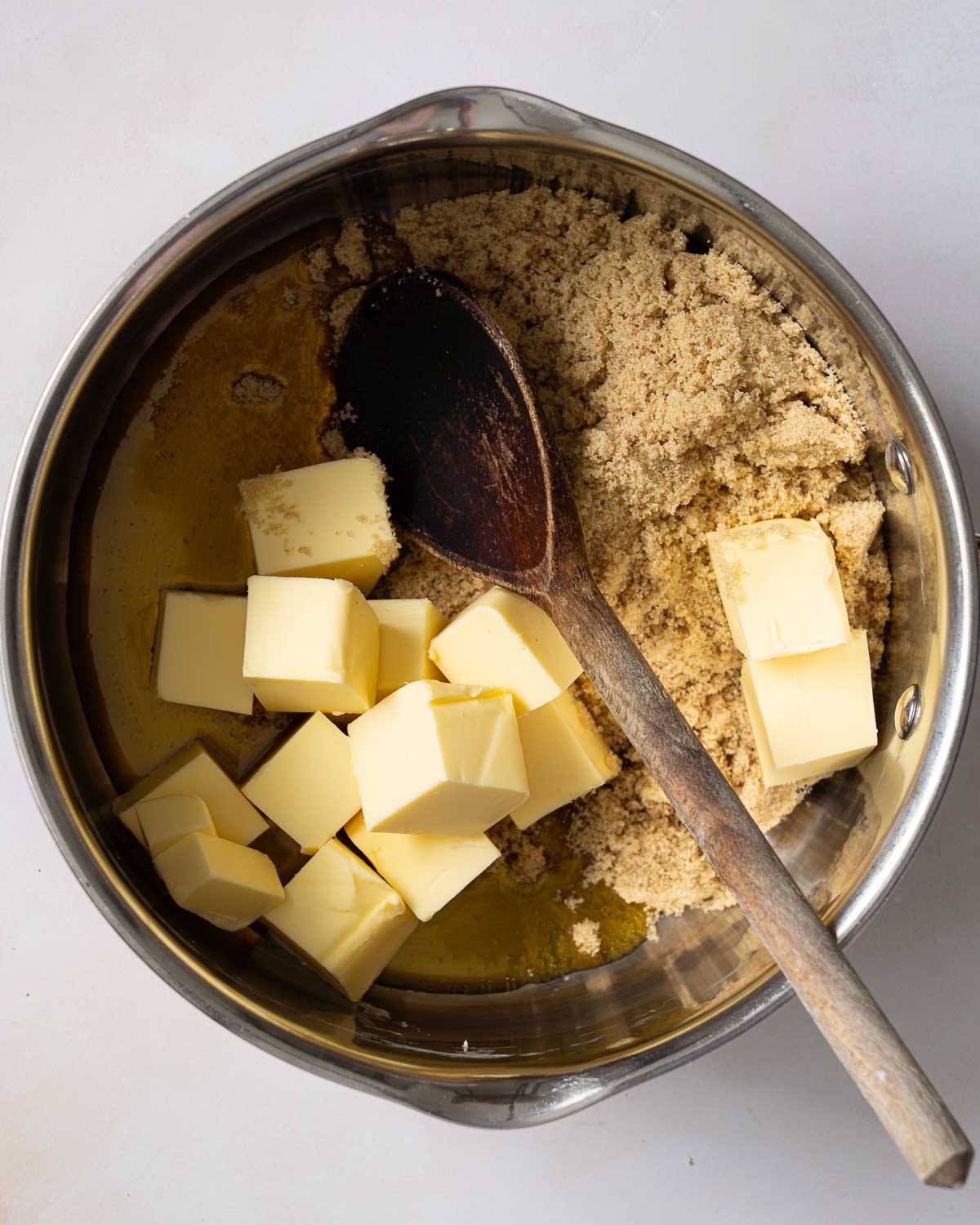 Butter, golden syrup and light brown sugar n a saucepan with a wooden spoon.