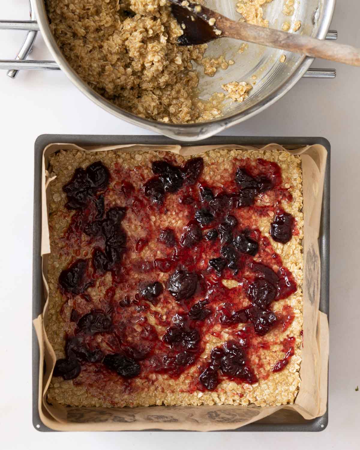 Jam spread over a layer of flapjack mixture in a baking tin.