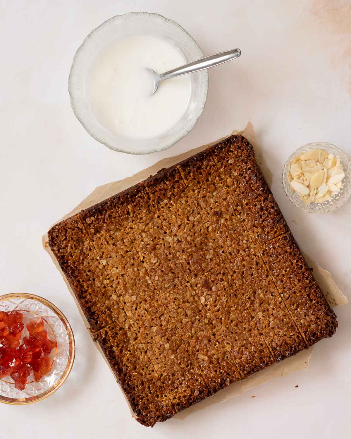 Freshly baked flapjack, scored and ready to be decorated with icing, cherries and almonds.