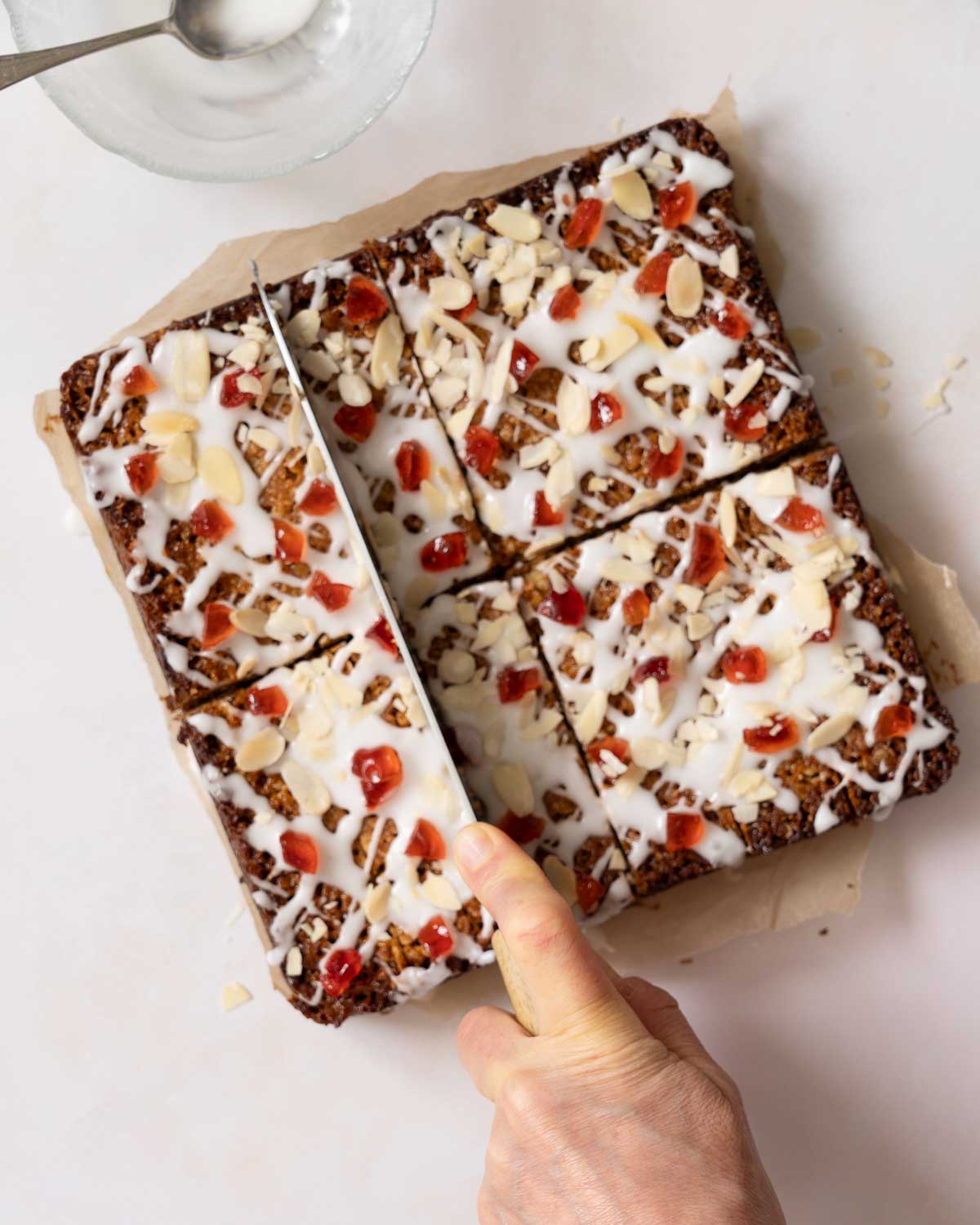 A person cutting slices of cherry and almond flapjack.