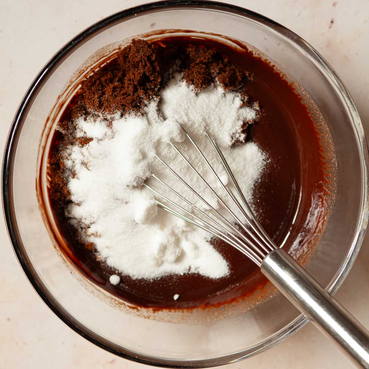 Caster sugar and muscovado sugar in a bowl with melted chocolate and a balloon whisk.