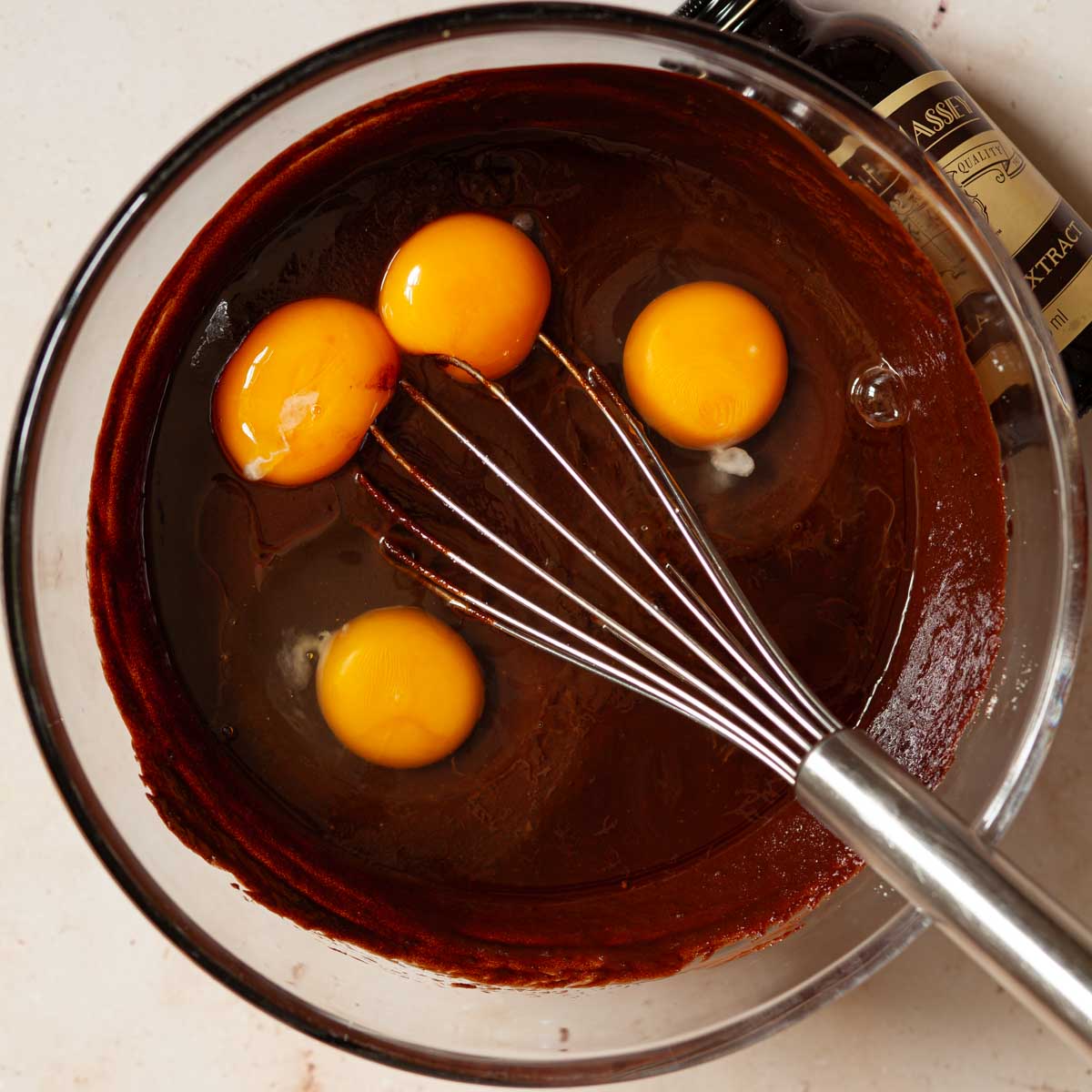 Eggs in a mixing bowl with chocolate brownie batter and a balloon whisk.