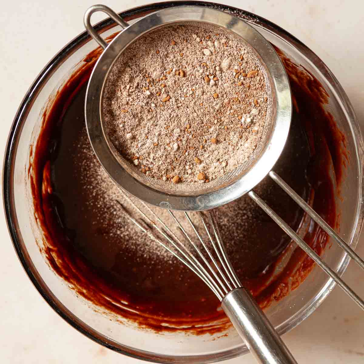 Flour, cocoa and espresso powder being sieved into brownie batter.