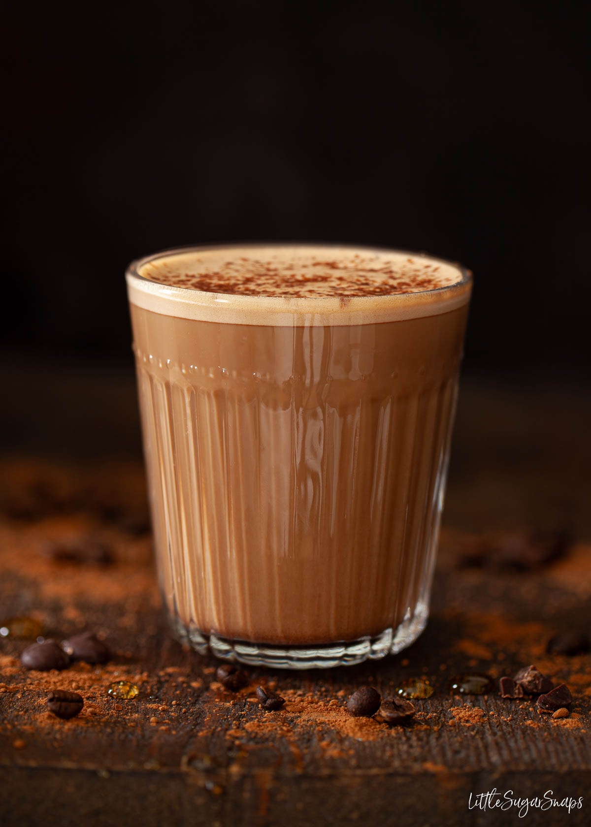 Salted caramel mocha latte in a glass mug with coffee beans on a wooden table.