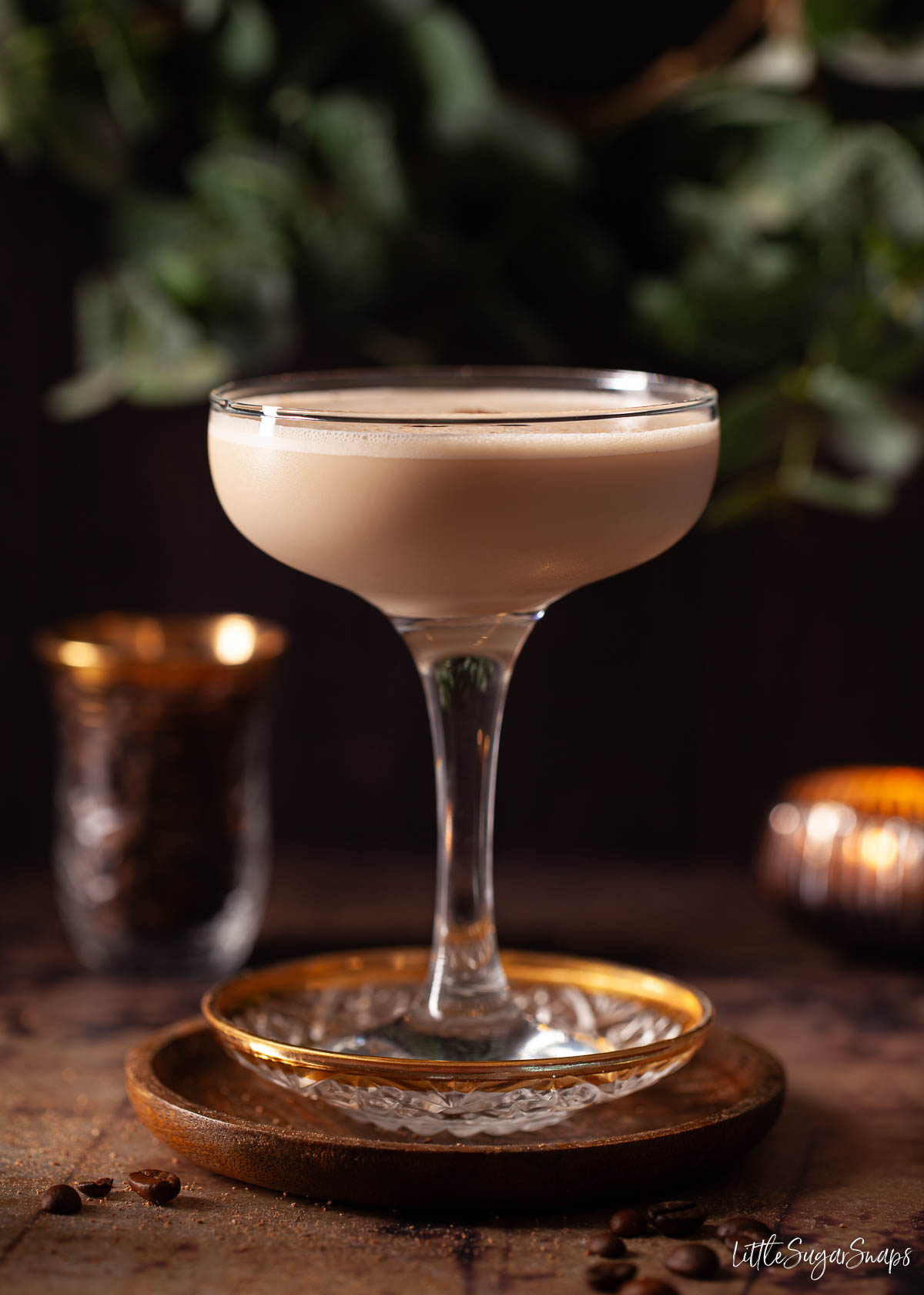 A creamy brandy cocktail in a dark setting with coffee beans and a candle in the background.