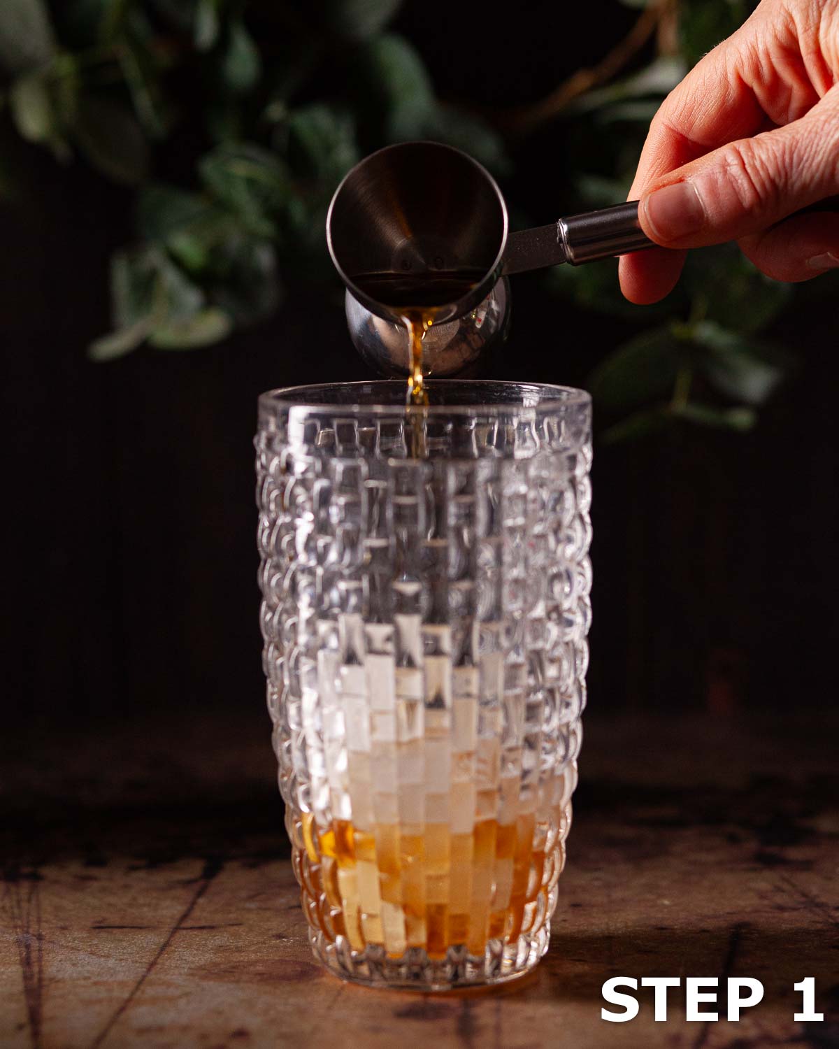 Person pouring brandy into an ice-filled cocktail shaker.