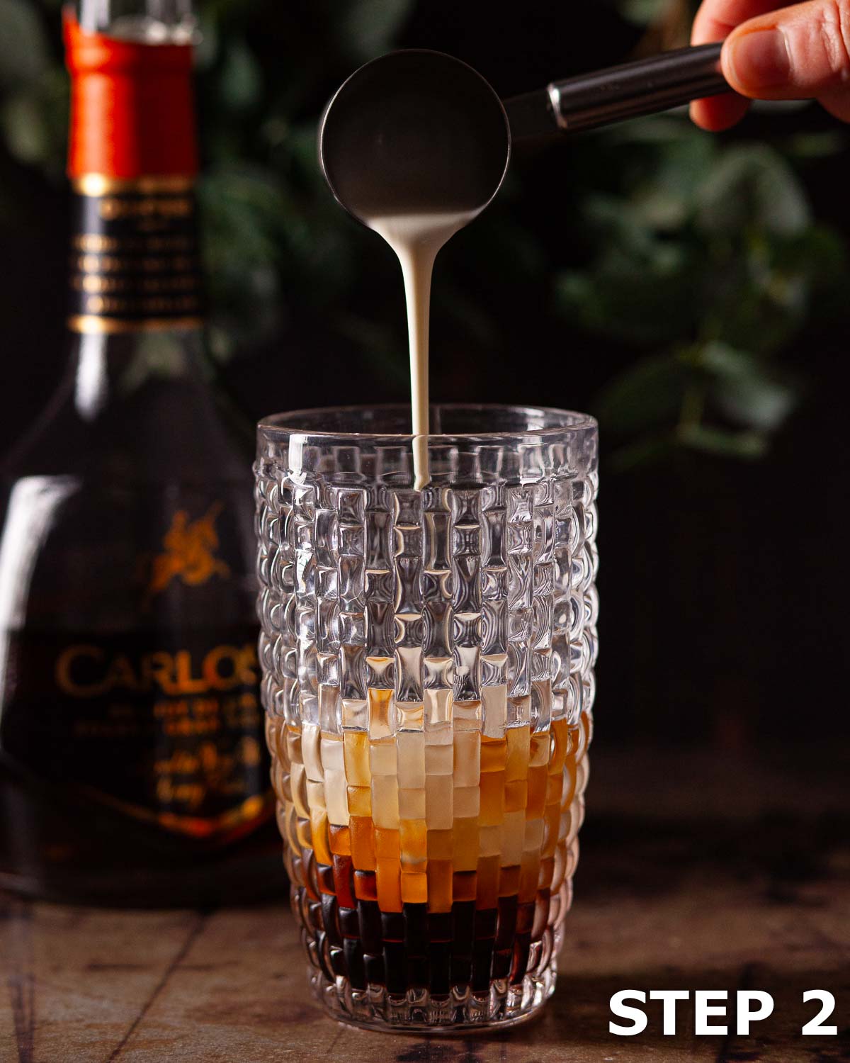 A person pouring cream into a cocktail shaker holding ice, coffee liqueur and brandy.