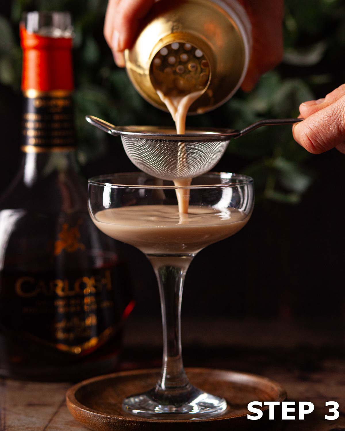 A person double straining a creamy coffee Alexander cocktail into a cocktail glass.