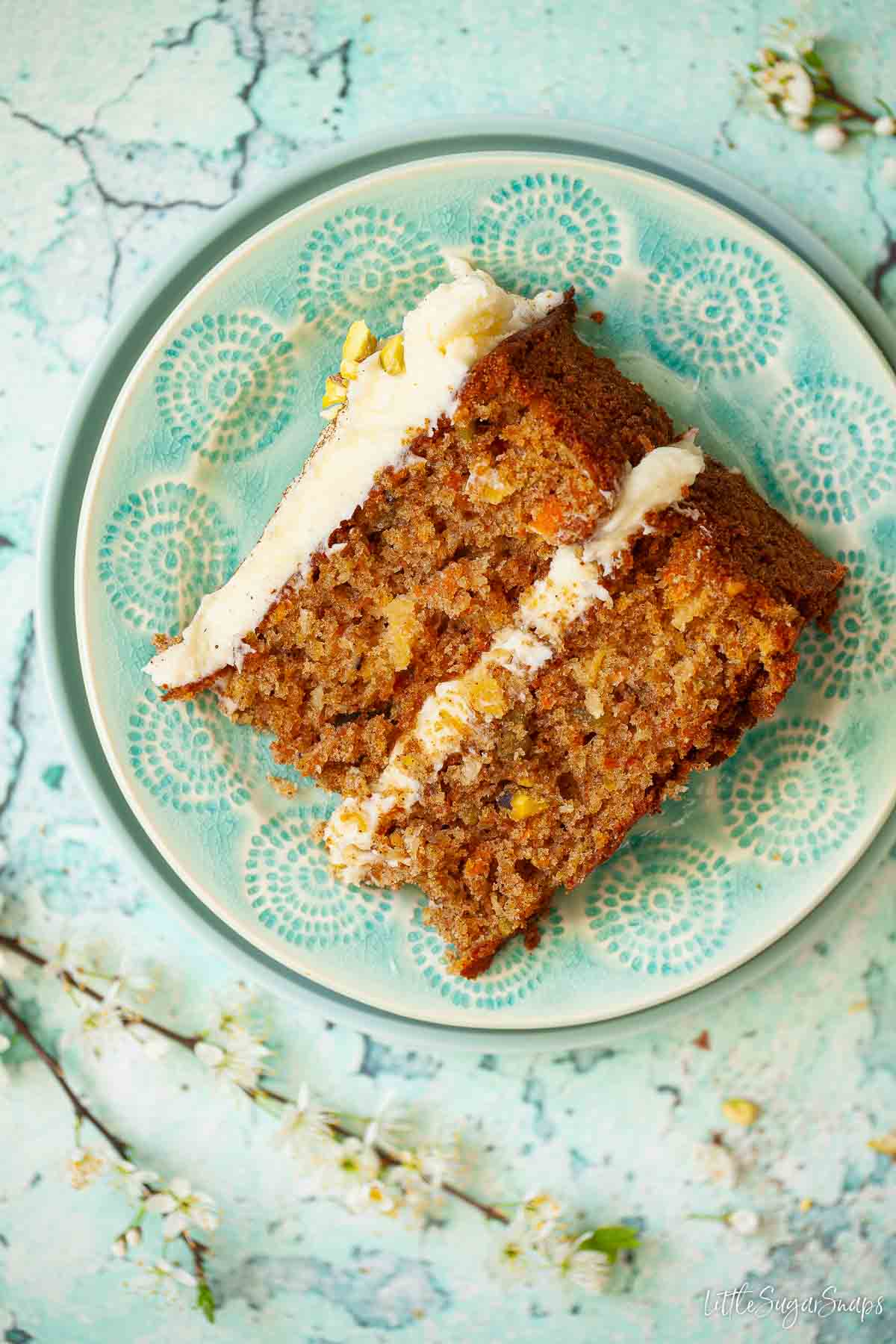 A slice of pistachio, carrot and pineapple cake with cream cheese frosting on a plate.
