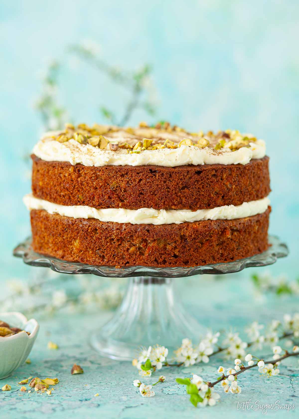 Whole carrot and pineapple cake with coconut on a cake stand.