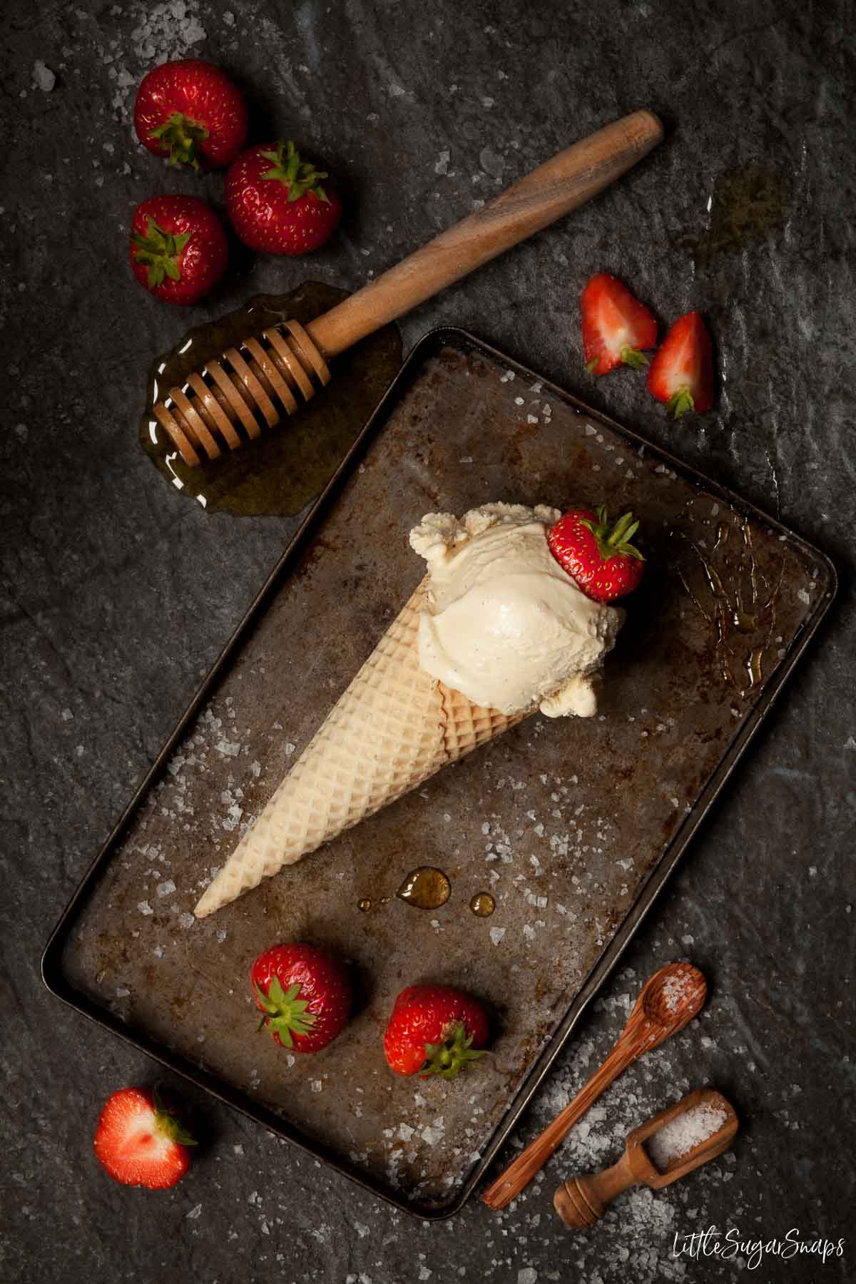 Honey ice cream with sea salt in a cone with strawberries alongside.