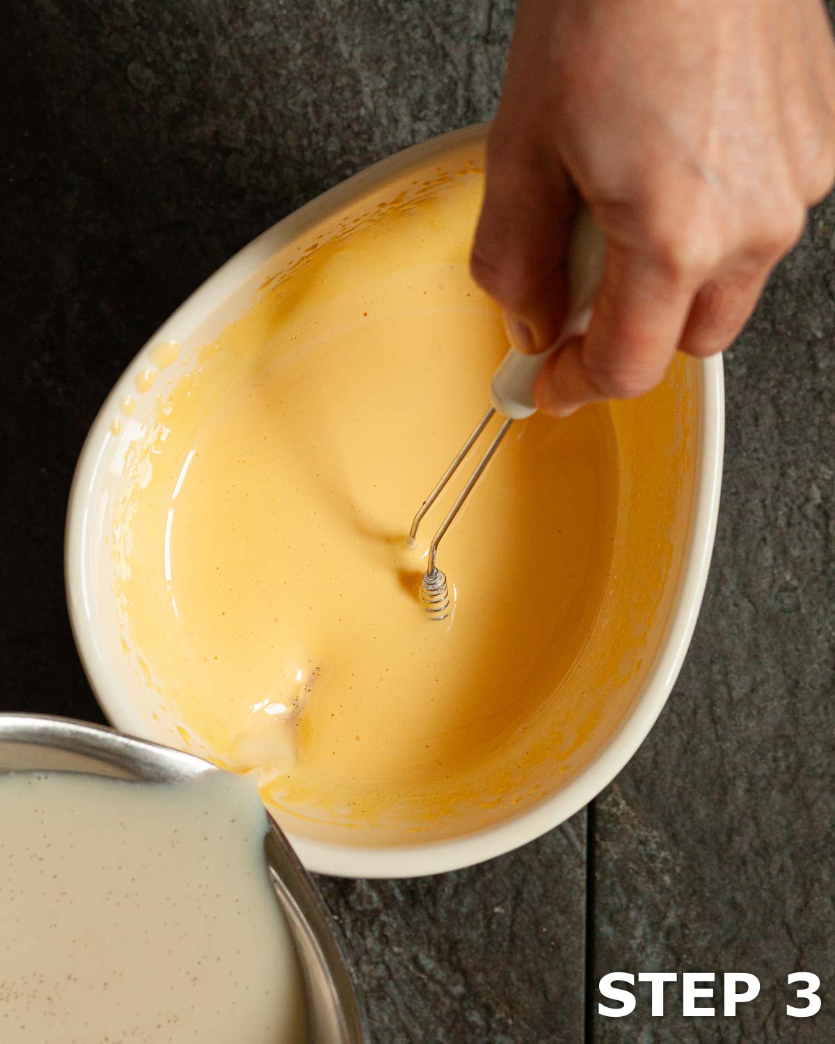 Person pouring and whisking milk into creamed egg yolks and sugar.