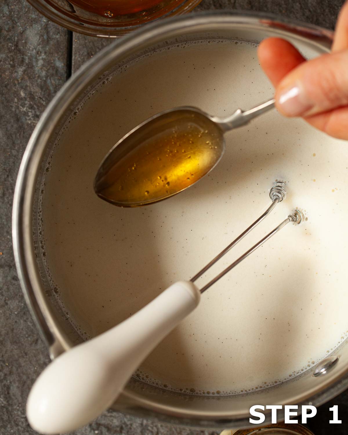 Honey being spooned into hot milk in a saucepan.