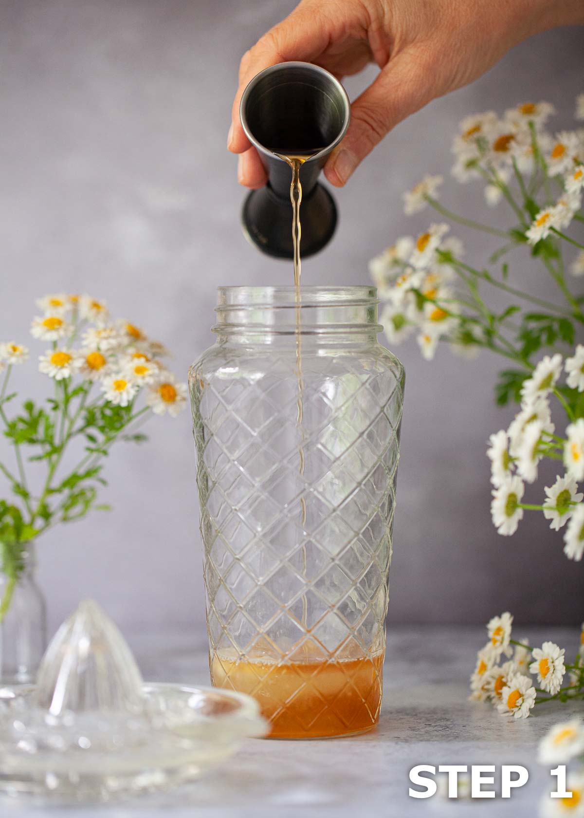 A person pouring alcohol from a jigger into a cocktail shaker.