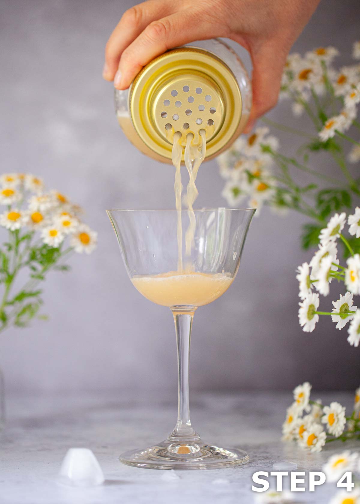 A person straining an Amaretto and bourbon cocktail into a sours glass.