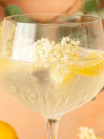Elderflower gin & tonic garnished with lemon wedges and elderflowers.