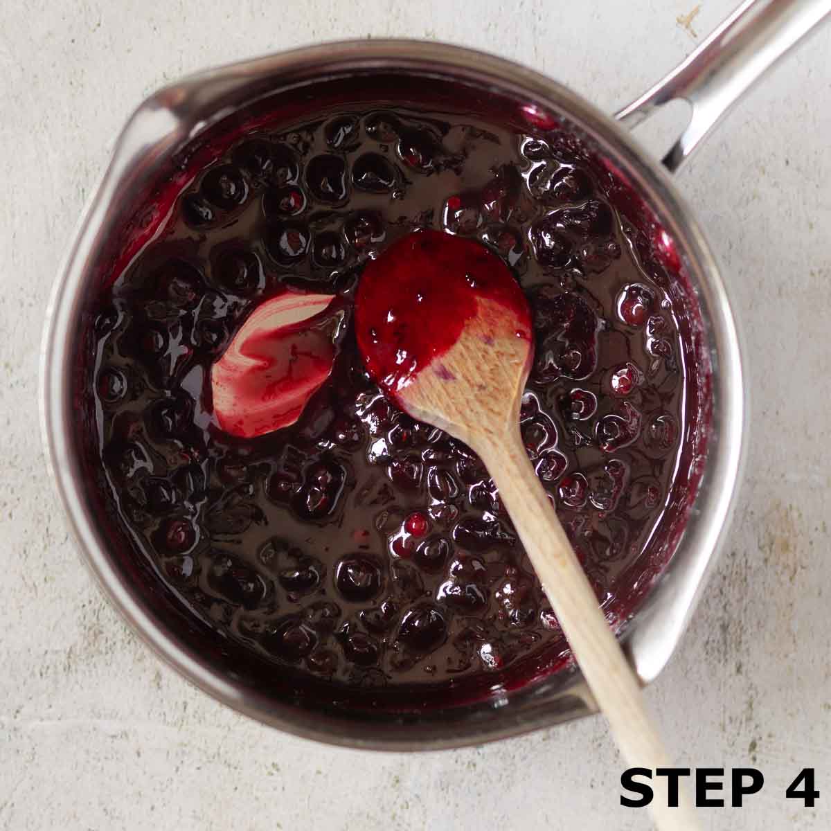 Blackcurrant compote in a pan with a wooden spoon.