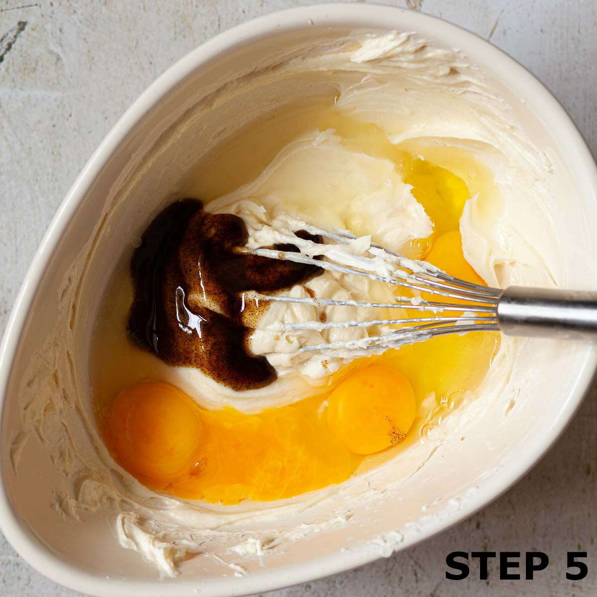 Eggs, vanilla bean paste and cream cheese in a mixing bowl with a balloon whisk.