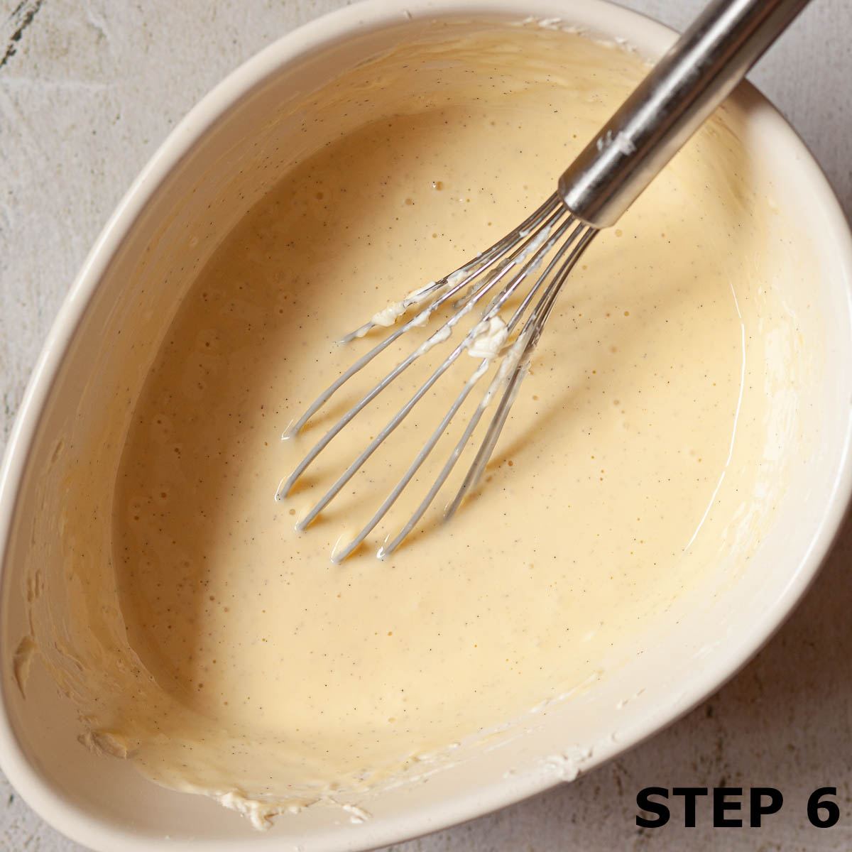 Vanilla cheesecake filling in a bowl with a balloon whisk.