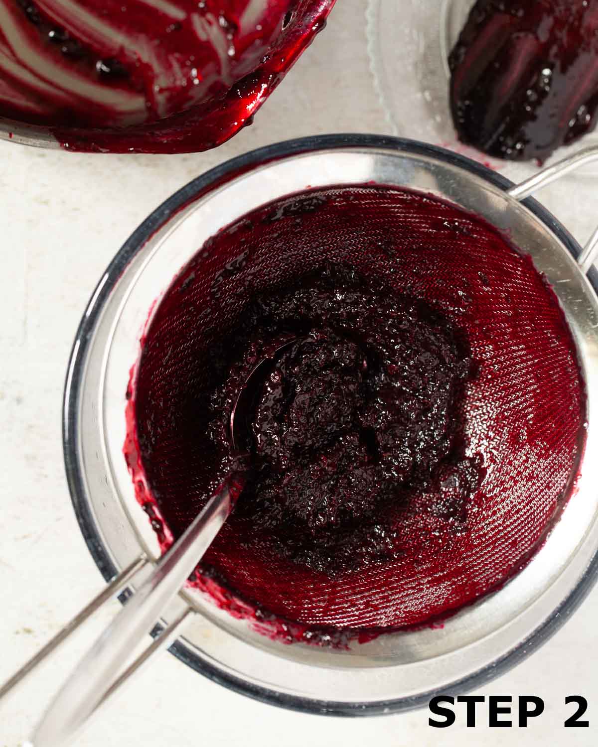 Blackcurrant compote being pushed through a sieve to make puree.