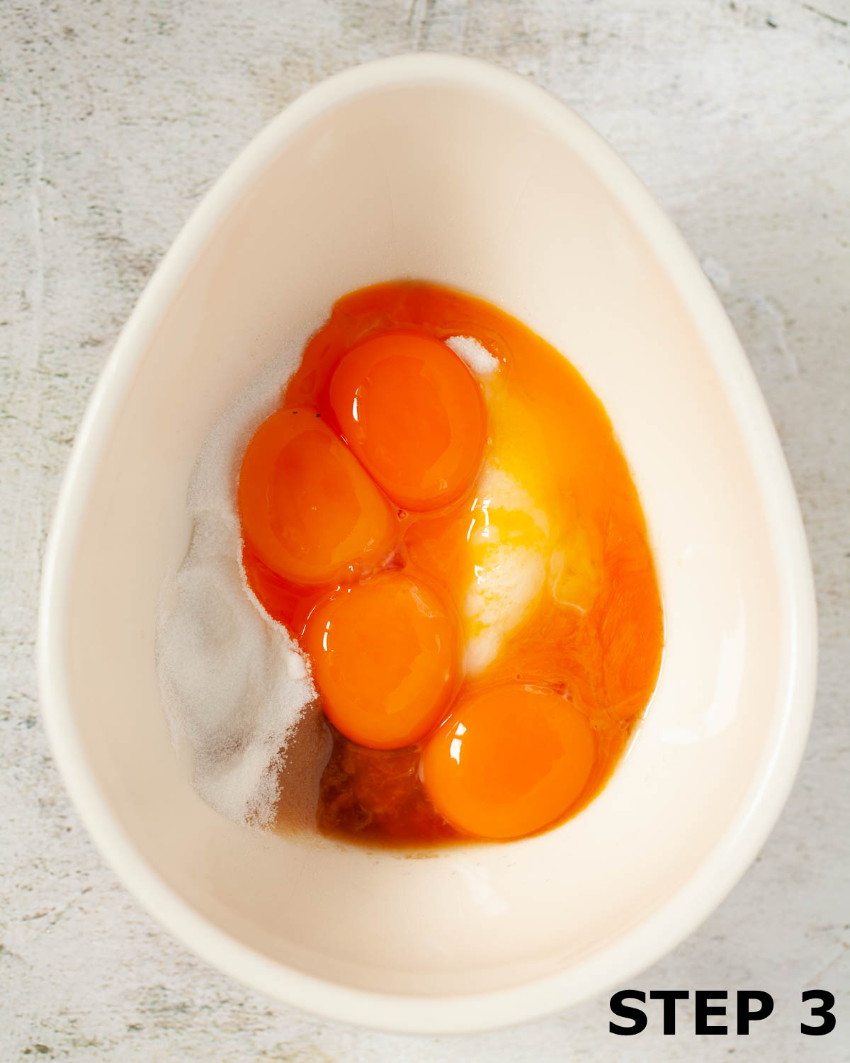 Egg yolks, sugar and vanilla in an egg-shaped mixing bowl.