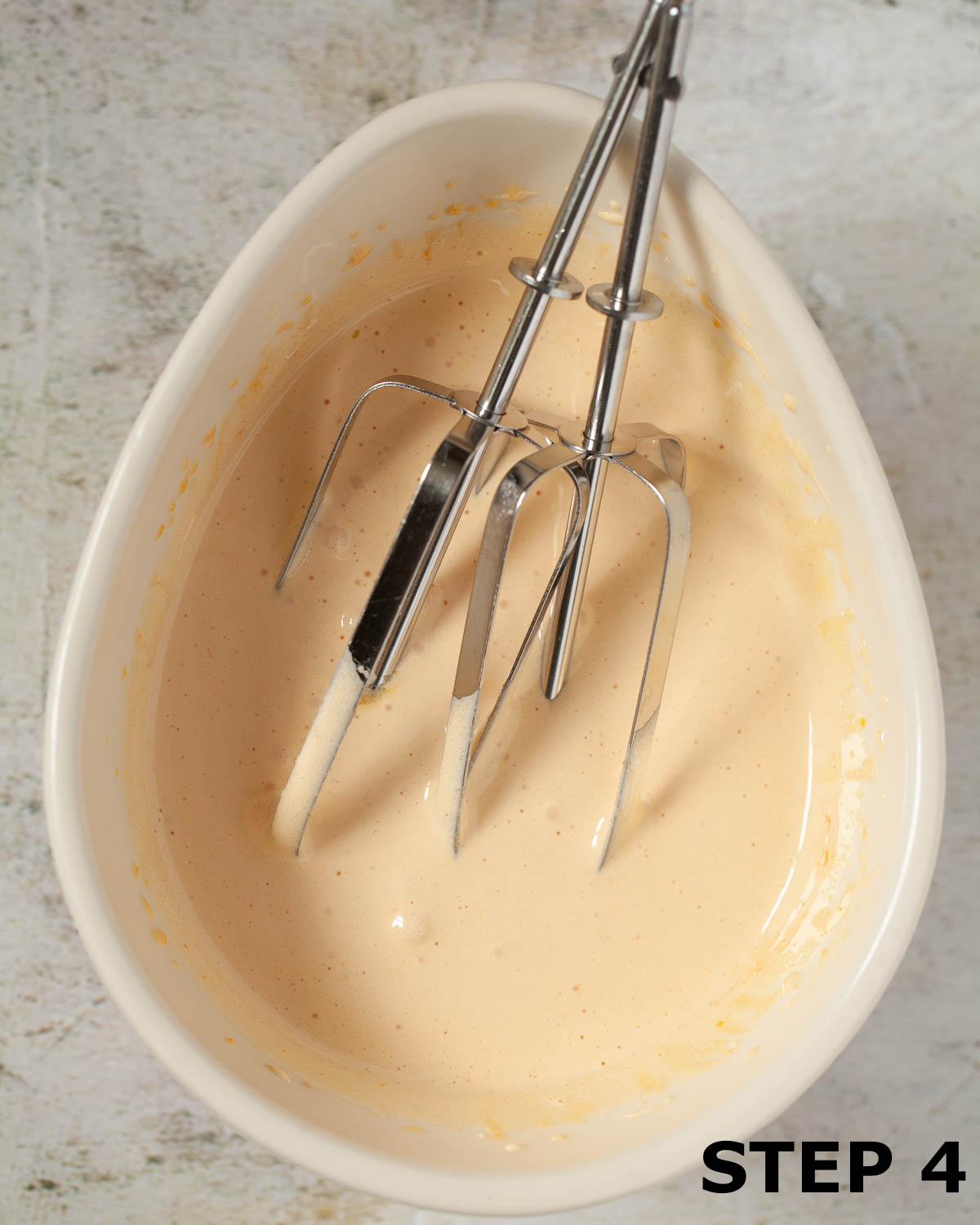 Electric beaters in a bowl of egg yolk and sugar that have been whisked until thick.