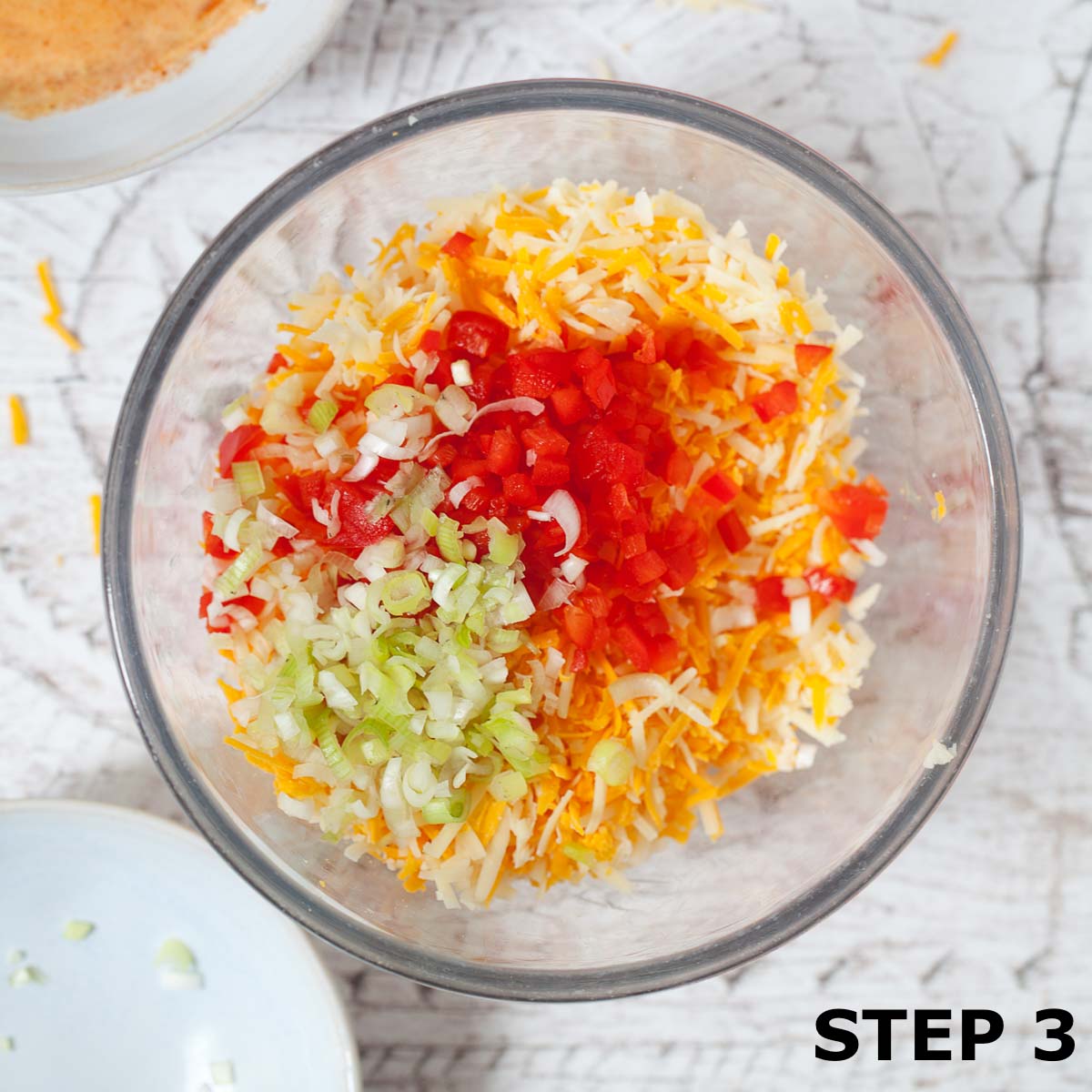 Grated cheese, chopped red pepper and chopped salad onion in a bowl.