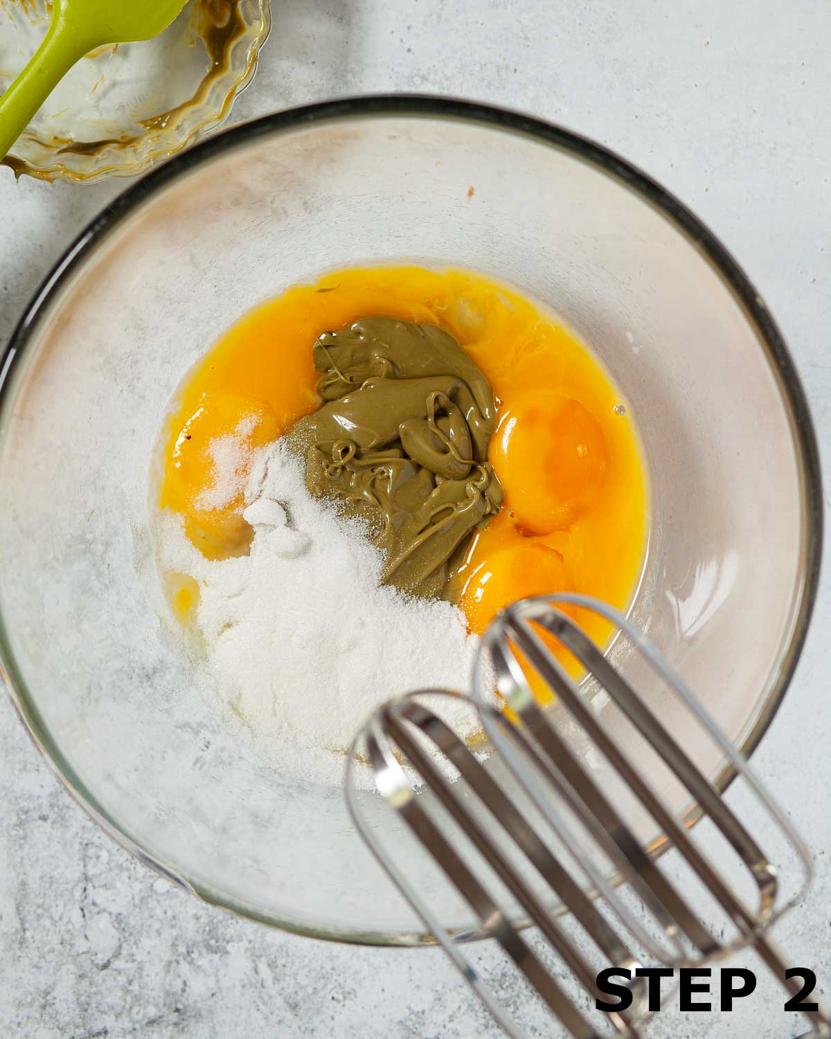 Eggs, pistachio creme and caster sugar in a bowl about to be mixed together with electric beaters.