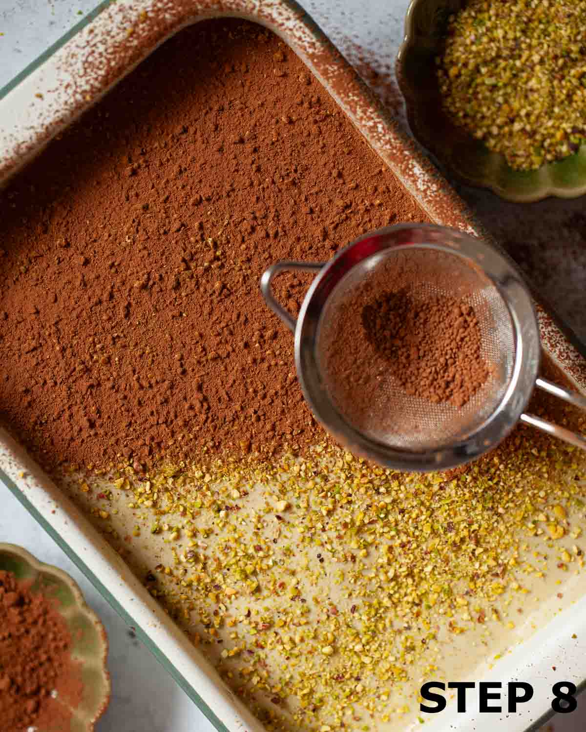 Cocoa powder being sieved over pistachio tiramisu.