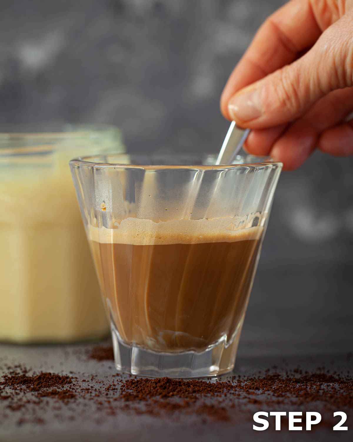 A person stirring condensed milk into espresso coffee.