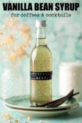 A bottle of vanilla bean syrup on a plate with vanilla pods with text overlay.