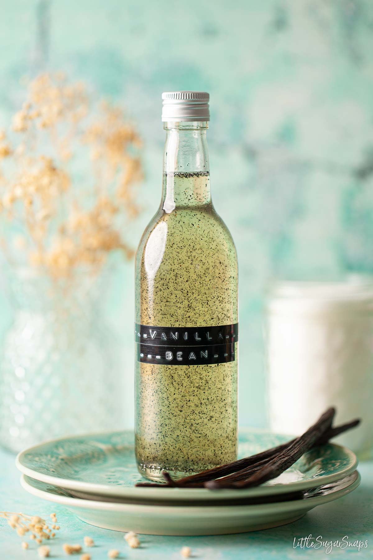 A bottle of vanilla bean syrup for coffee on a plate with vanilla pods.