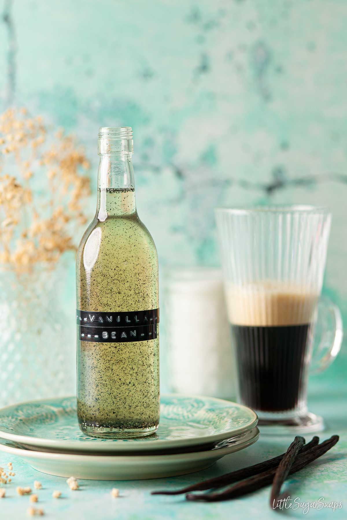 A bottle of vanilla bean syrup with espresso coffee in a glass in the background.