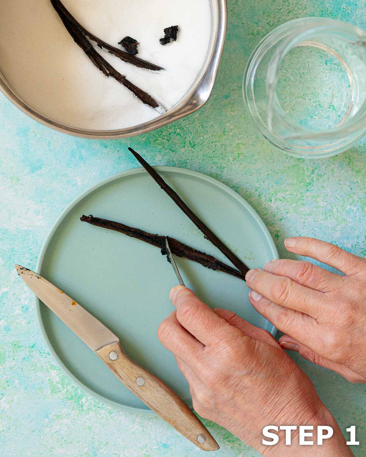 A person scraping the beans from a vanilla pod before adding them to a pan with sugar and water.