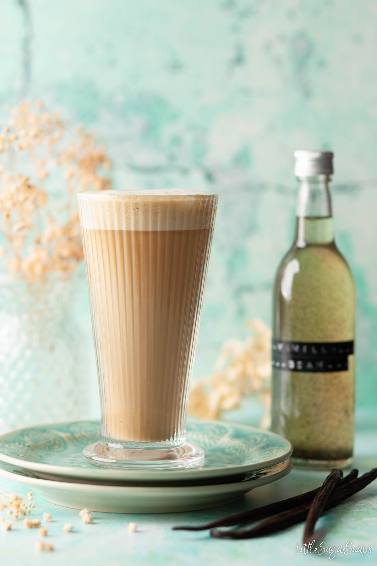 A vanilla latte with vanilla pods and a bottle of vanilla bean syrup.