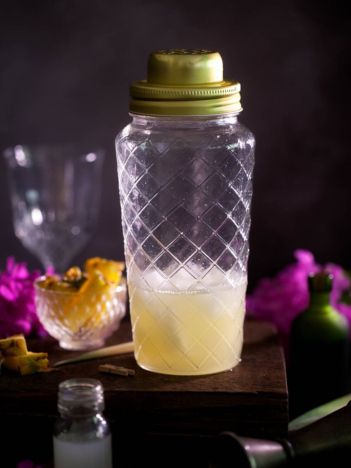 A gin and pineapple juice cocktail in a glass shaker freshly shaken