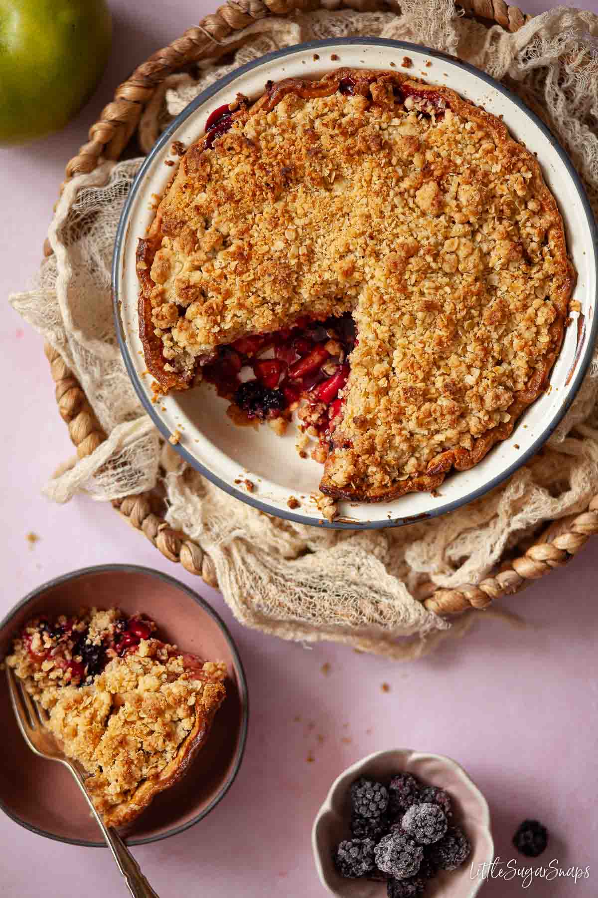Apple and blackberry pie with crumble topping with a slice served in a bowl.