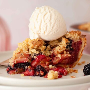 A slice and apple and blackberry pie with a ball of vanilla ice cream on top.