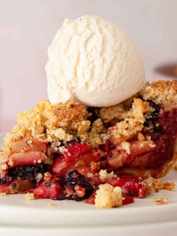 A slice and apple and blackberry pie with a ball of vanilla ice cream on top.