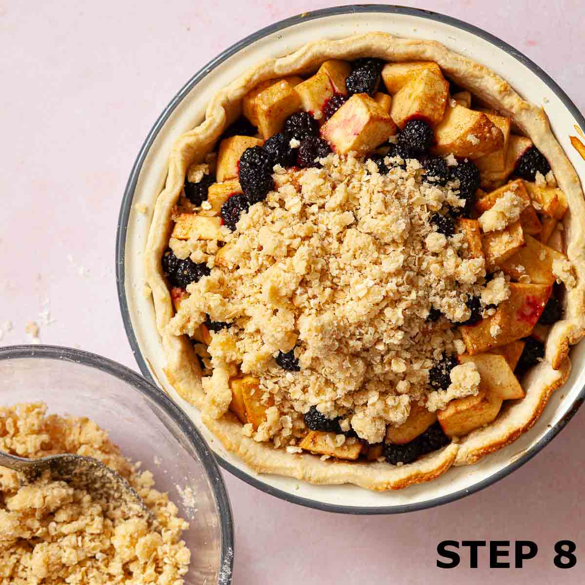 Crumble topping being spread over fruit in a pie dish.