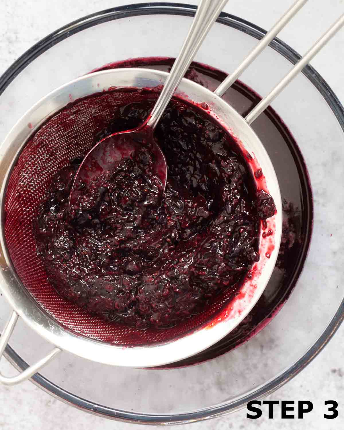 Blackcurrant sauce being pushed through a sieve suspended over a bowl.